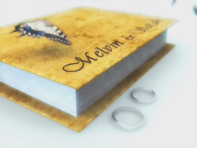 The butterfly flies to a book with a pair of wedding ring beside it 
